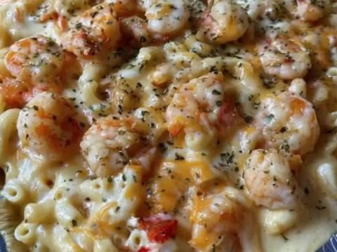 Baked seafood macaroni and cheese in an aluminum pan topped with seared shrimp and fresh herbs.