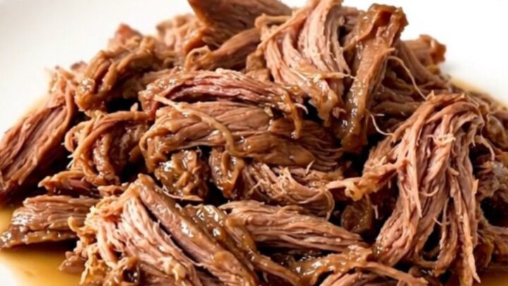 A succulent beef chuck roast sitting in a dark slow cooker, surrounded by aromatic garlic and herbs.