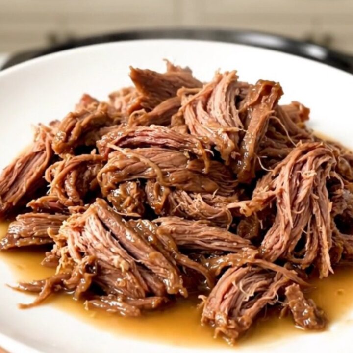 A succulent beef chuck roast sitting in a dark slow cooker, surrounded by aromatic garlic and herbs.