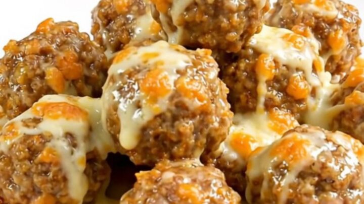 A white plate filled with steaming, glossy turkey meatballs coated in a creamy garlic parmesan sauce with melted cheese.