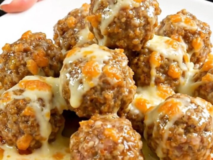 A white plate filled with steaming, glossy turkey meatballs coated in a creamy garlic parmesan sauce with melted cheese.