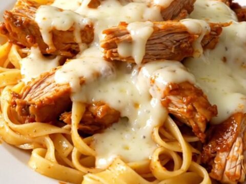 A close-up of creamy roasted red pepper alfredo chicken thighs served over fettuccine on a white plate.