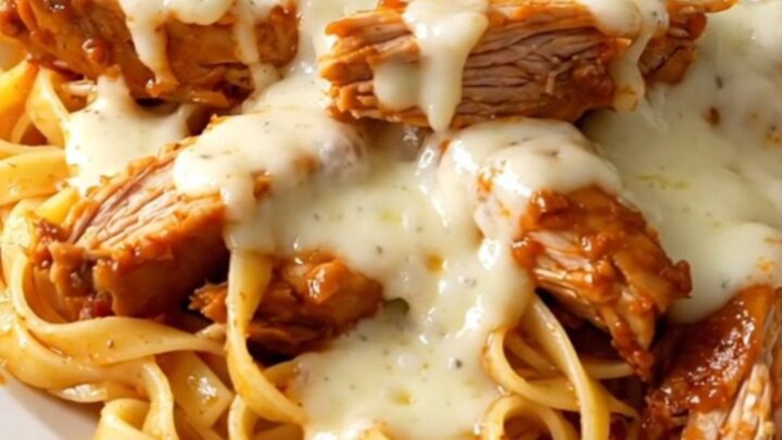 A close-up of creamy roasted red pepper alfredo chicken thighs served over fettuccine on a white plate.