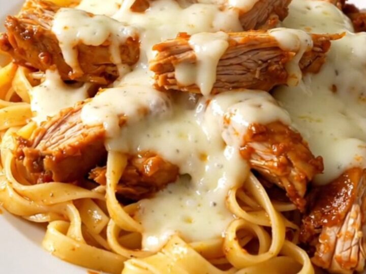 A close-up of creamy roasted red pepper alfredo chicken thighs served over fettuccine on a white plate.