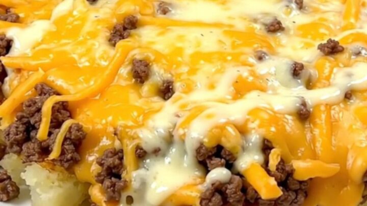 A steaming, creamy cheesy hamburger and potato casserole served in a slow cooker on a white speckled countertop.