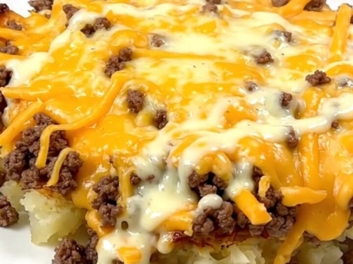A steaming, creamy cheesy hamburger and potato casserole served in a slow cooker on a white speckled countertop.