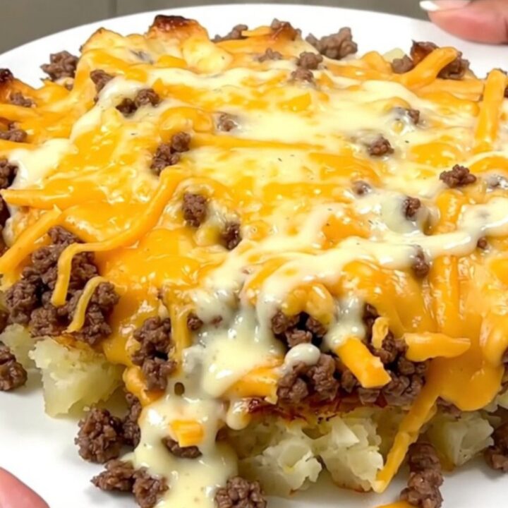 A steaming, creamy cheesy hamburger and potato casserole served in a slow cooker on a white speckled countertop.