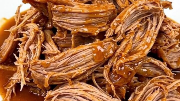 A close-up shot of a tender, shredded Cajun butter pork roast served on a white plate with visible steam.