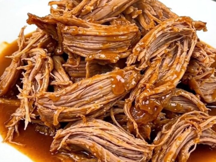 A close-up shot of a tender, shredded Cajun butter pork roast served on a white plate with visible steam.
