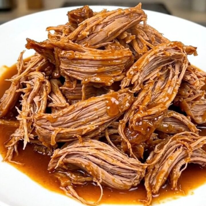 A close-up shot of a tender, shredded Cajun butter pork roast served on a white plate with visible steam.
