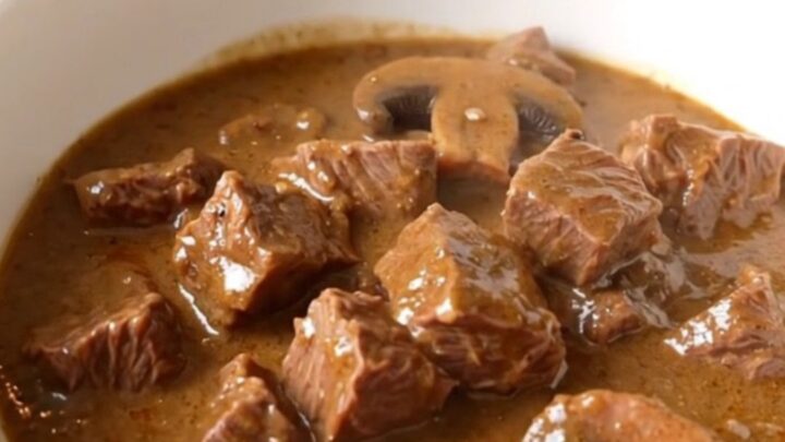 A steaming bowl of creamy mushroom beef stew served in a white bowl with a spoon.