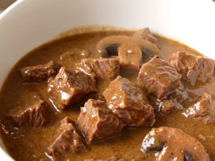 A steaming bowl of creamy mushroom beef stew served in a white bowl with a spoon.