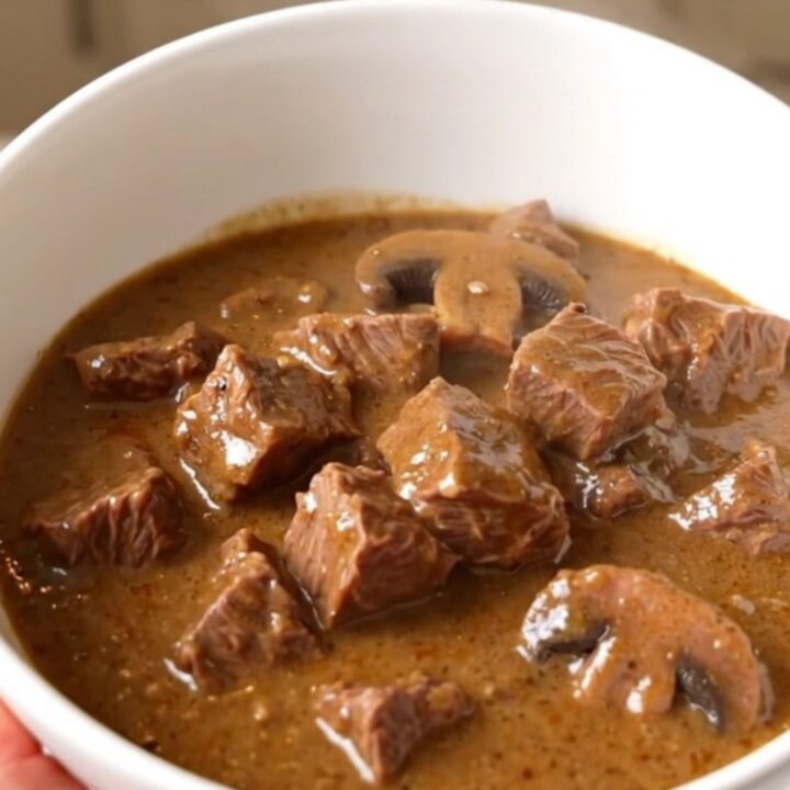 A steaming bowl of creamy mushroom beef stew served in a white bowl with a spoon.