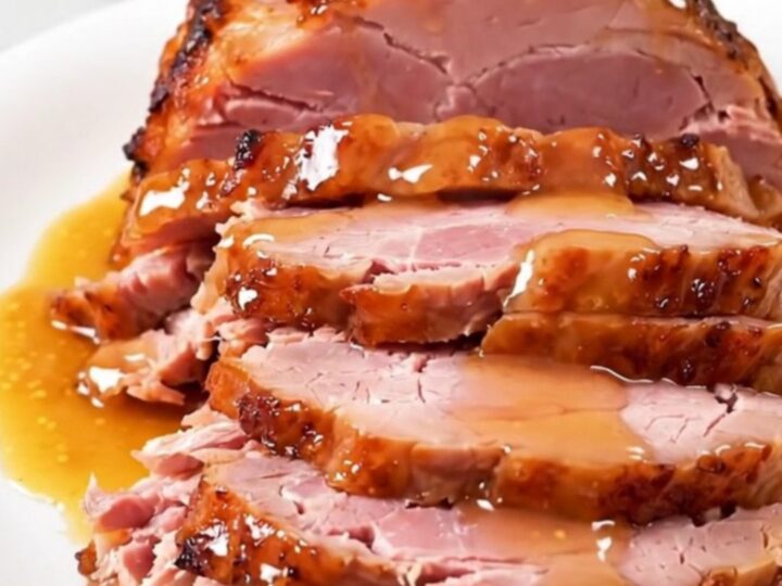 A whole, glazed spiral-cut ham sitting in a slow cooker, glistening with an apricot and Dijon mustard glaze.