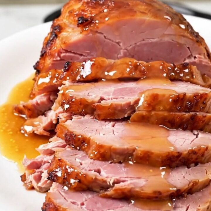 A whole, glazed spiral-cut ham sitting in a slow cooker, glistening with an apricot and Dijon mustard glaze.