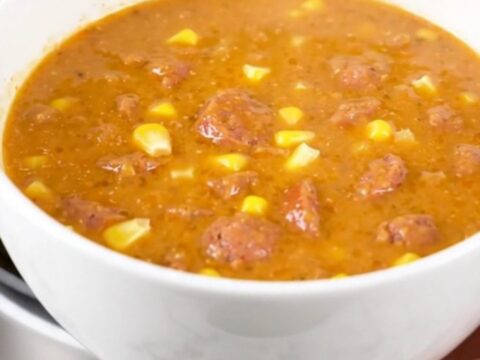 A steaming bowl of creamy Cajun corn and sausage chowder on a white surface.