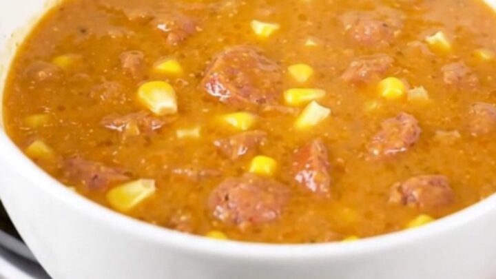 A steaming bowl of creamy Cajun corn and sausage chowder on a white surface.