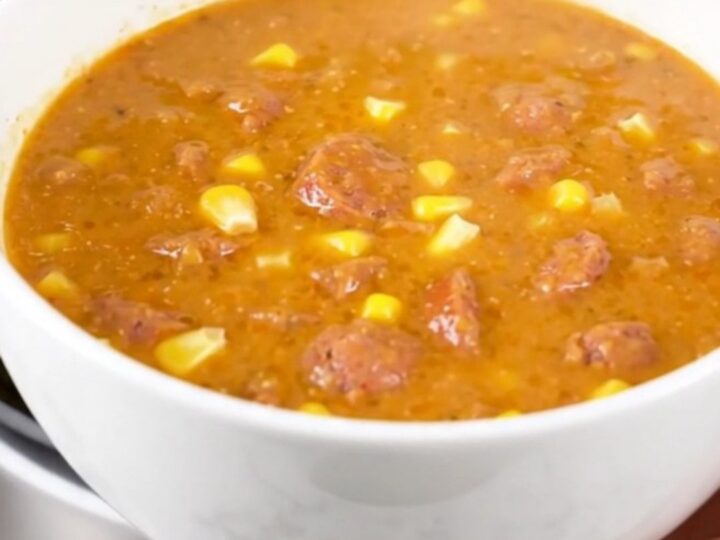 A steaming bowl of creamy Cajun corn and sausage chowder on a white surface.