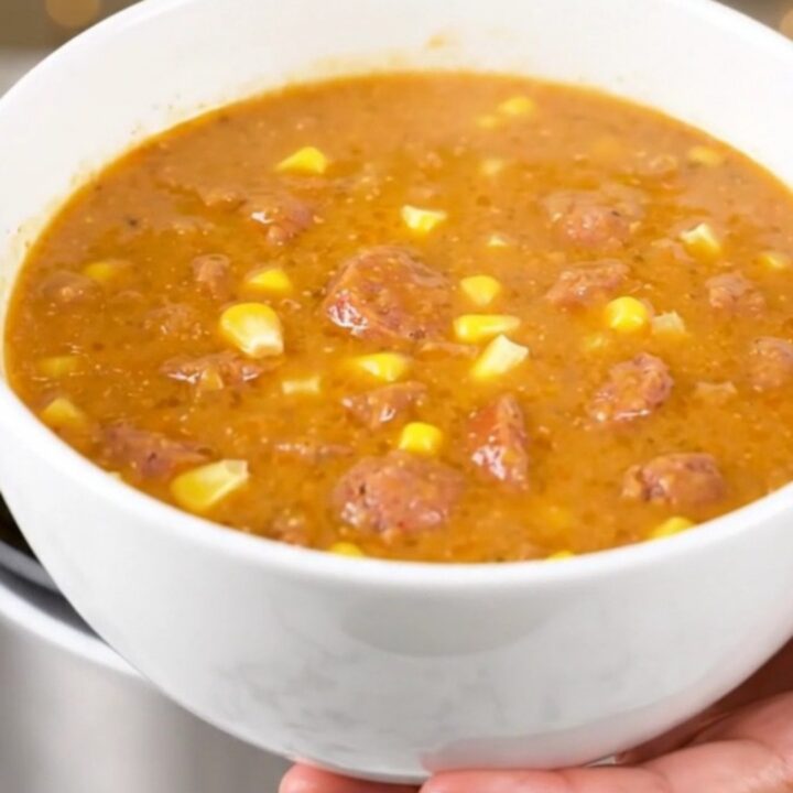 A steaming bowl of creamy Cajun corn and sausage chowder on a white surface.