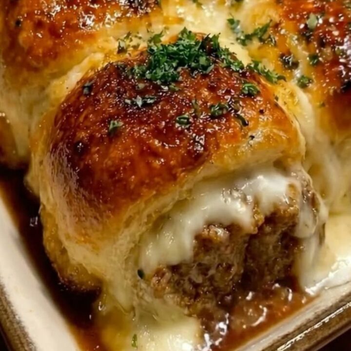 A warm baking dish filled with golden brown, glossy garlic butter meatball sliders showing a dramatic cheese pull.