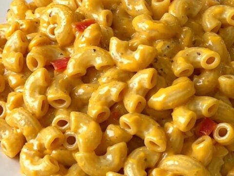 A close-up shot of a creamy, steaming bowl of Cajun macaroni with visible red bell peppers.