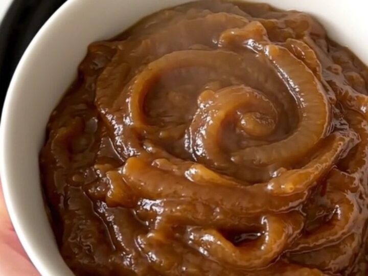 A warm, creamy caramelized onion dip in a white bowl, showing a smooth and glossy texture with visible onion pieces.