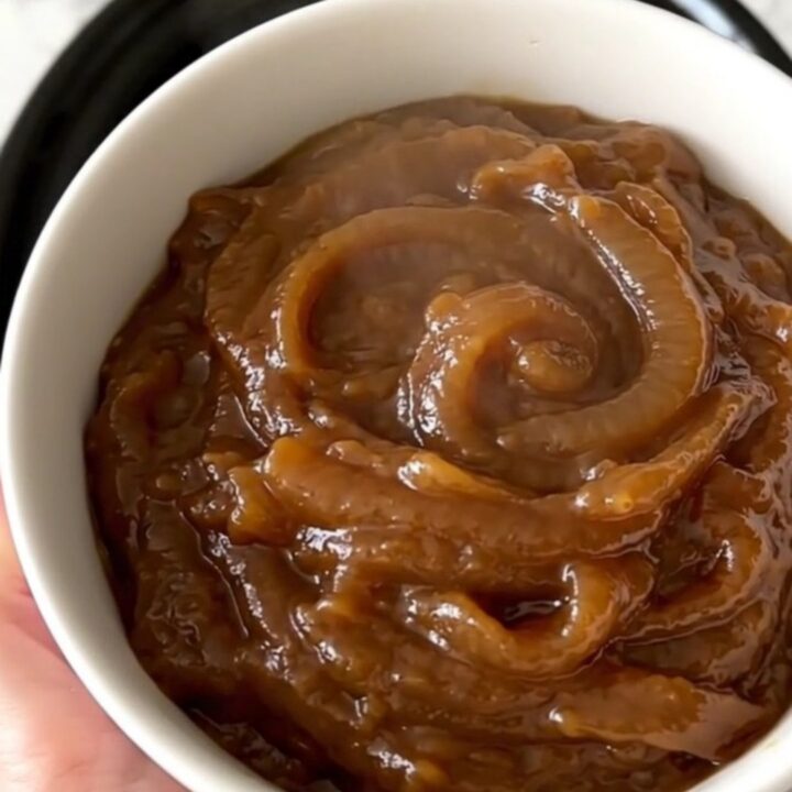 A warm, creamy caramelized onion dip in a white bowl, showing a smooth and glossy texture with visible onion pieces.