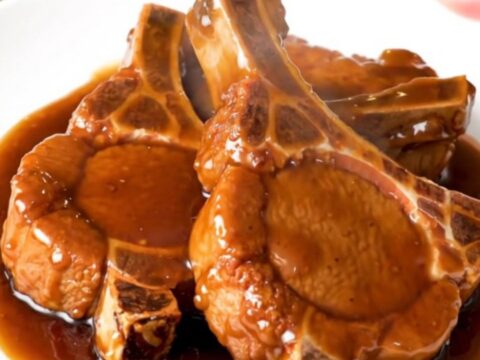 A close-up of tender General Tso pork chops glazed in a dark, sticky hoisin sauce on a white plate.