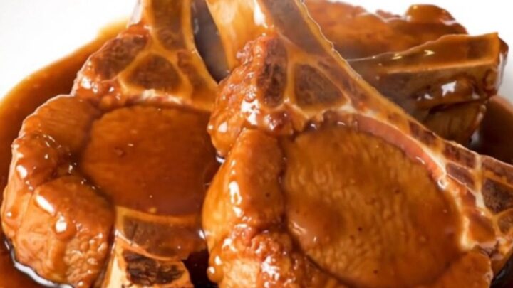 A close-up of tender General Tso pork chops glazed in a dark, sticky hoisin sauce on a white plate.