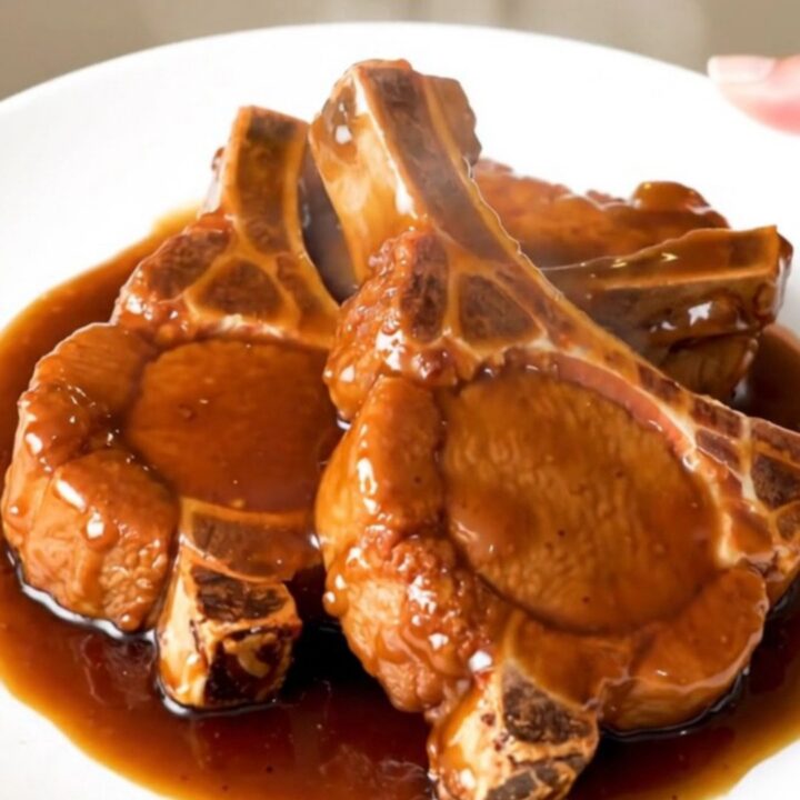 A close-up of tender General Tso pork chops glazed in a dark, sticky hoisin sauce on a white plate.