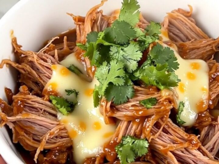 A white bowl filled with shredded pork, corn, and red enchilada sauce, topped with melted shredded cheddar cheese.