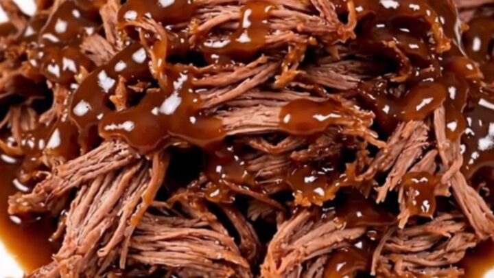 A close-up of tender, glossy barbecue shredded beef piled high on a white plate.