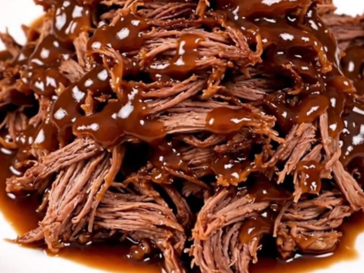 A close-up of tender, glossy barbecue shredded beef piled high on a white plate.