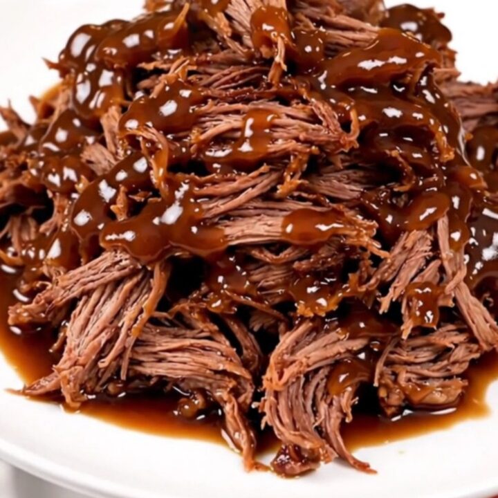 A close-up of tender, glossy barbecue shredded beef piled high on a white plate.