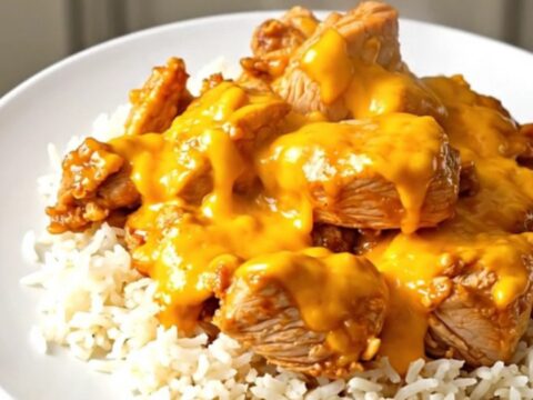 A top-down view of chicken thighs, broccoli, and cheddar sauce cooking in a black slow cooker on a speckled countertop.