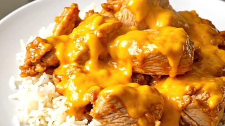 A top-down view of chicken thighs, broccoli, and cheddar sauce cooking in a black slow cooker on a speckled countertop.