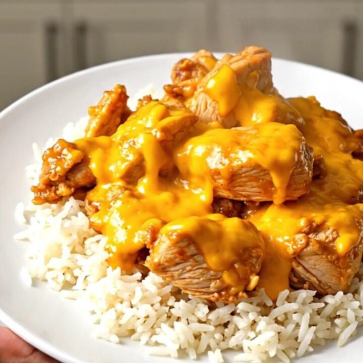 A top-down view of chicken thighs, broccoli, and cheddar sauce cooking in a black slow cooker on a speckled countertop.