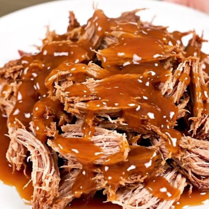 A plate of shredded sweet chili lime pulled pork with a glossy finish on a white plate.