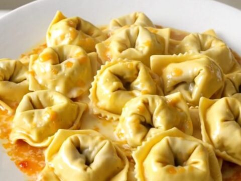 A glossy, steaming bowl of creamy garlic parmesan tortellini bake in a slow cooker.