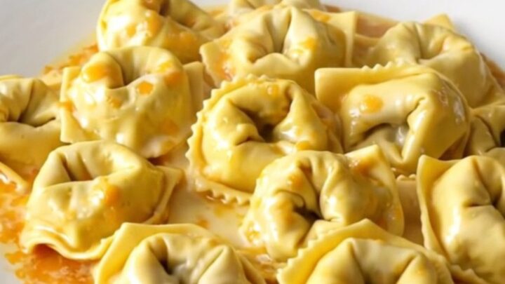 A glossy, steaming bowl of creamy garlic parmesan tortellini bake in a slow cooker.