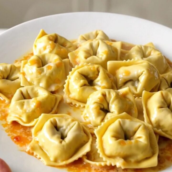 A glossy, steaming bowl of creamy garlic parmesan tortellini bake in a slow cooker.