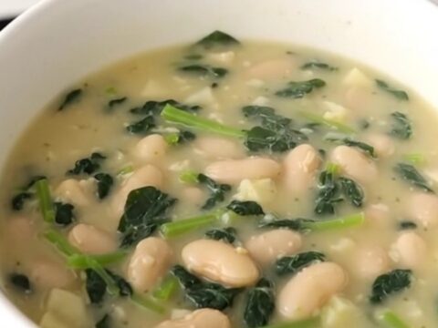 A rustic bowl of creamy white bean and spinach chowder with visible potato cubes and wilted greens.