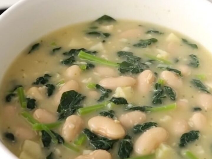 A rustic bowl of creamy white bean and spinach chowder with visible potato cubes and wilted greens.