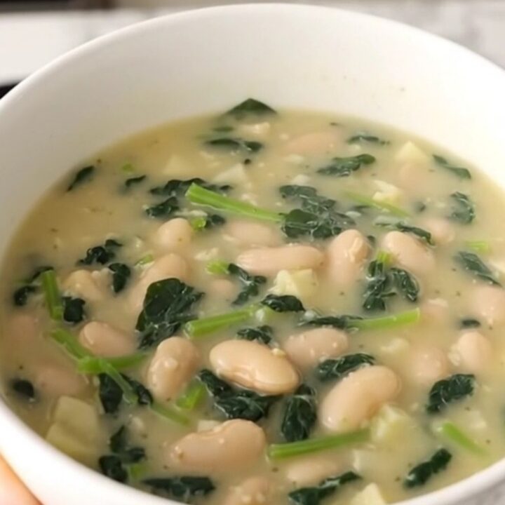 A rustic bowl of creamy white bean and spinach chowder with visible potato cubes and wilted greens.