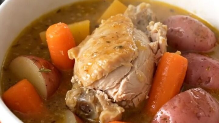 A steaming bowl of rosemary garlic chicken stew with chunks of chicken, red potatoes, and carrots in a rich broth.