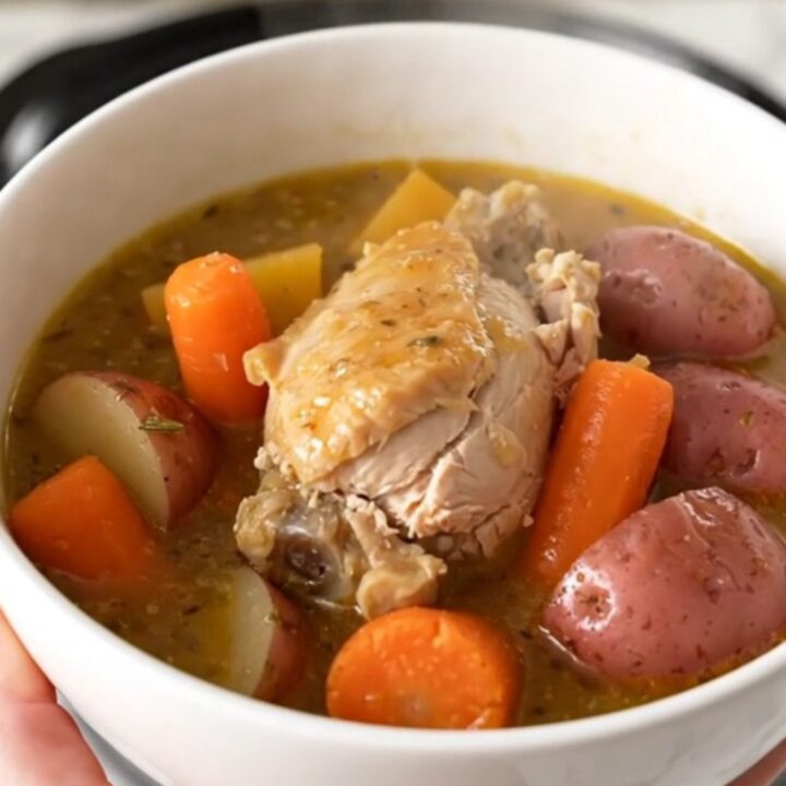 A steaming bowl of rosemary garlic chicken stew with chunks of chicken, red potatoes, and carrots in a rich broth.