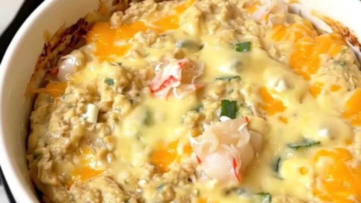 A close-up of a creamy, steaming hot crab dip in a white bowl with scallions.