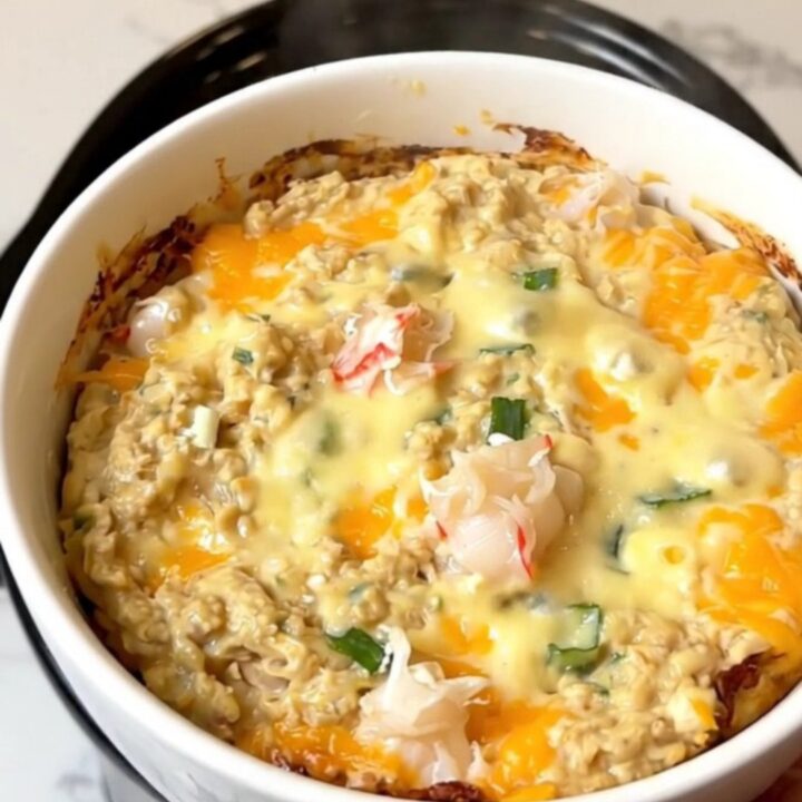 A close-up of a creamy, steaming hot crab dip in a white bowl with scallions.