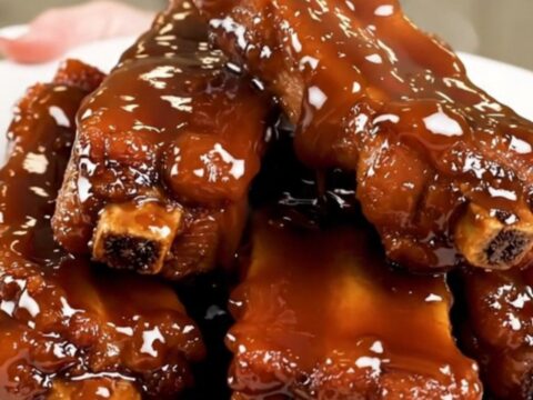 A plate of sticky, glossy glazed pork ribs steaming on a white plate.
