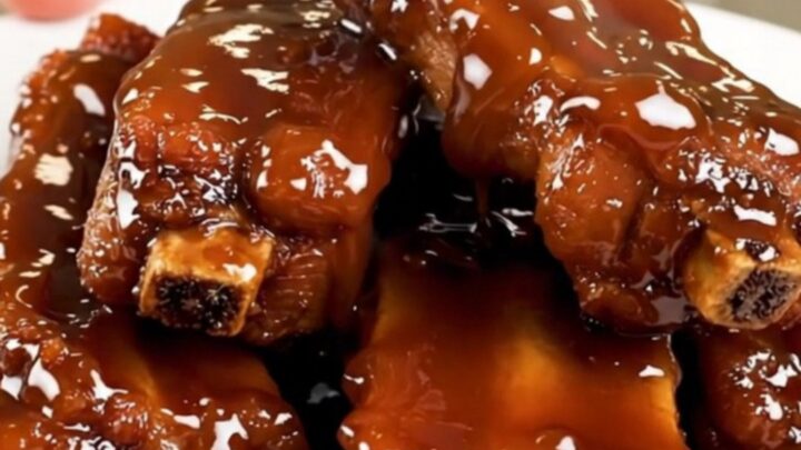 A plate of sticky, glossy glazed pork ribs steaming on a white plate.